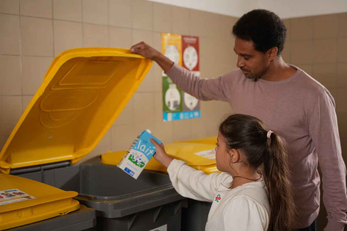 Un pÃ¨re et sa fille triant une brique de lait vide dans les bacs jaune de tri sÃ©lectif.