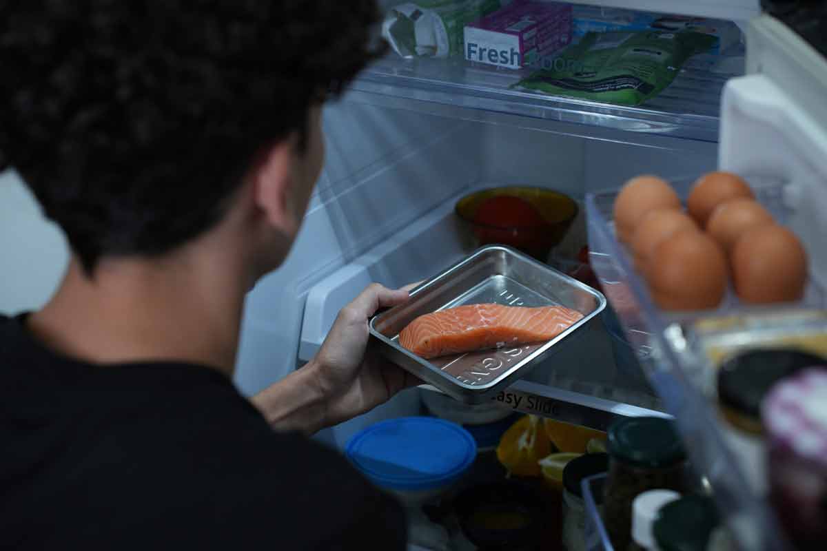 Un homme qui range du saumon, dans un emballage rÃ©employable dans un frigo.